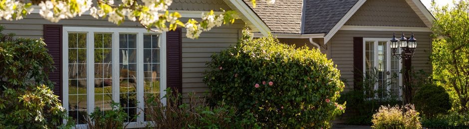 Beautiful suburban home in Spring, white windows with grilles and black shutters. Blossoming tree and bushes.